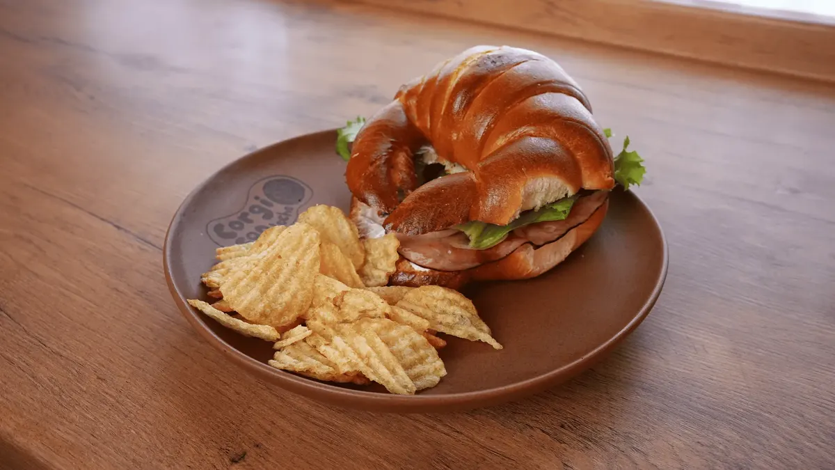 Croissant: Queso derretido, lechuga, cebolla caramelizada y tocino. Elige proteína y aderezo.